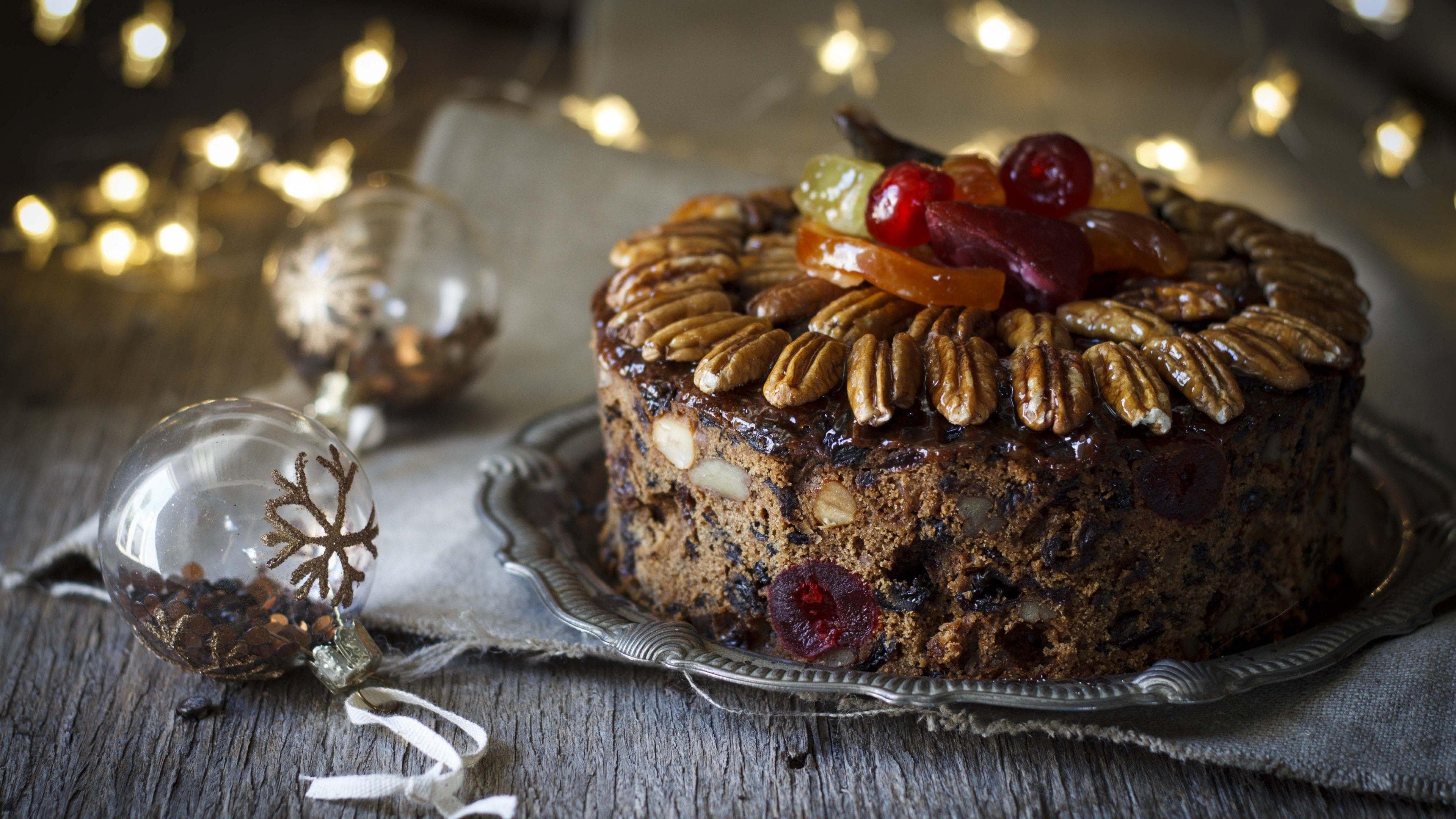 Festive fruitcake with nuts and candied fruit on a silver plate beside Christmas ornaments