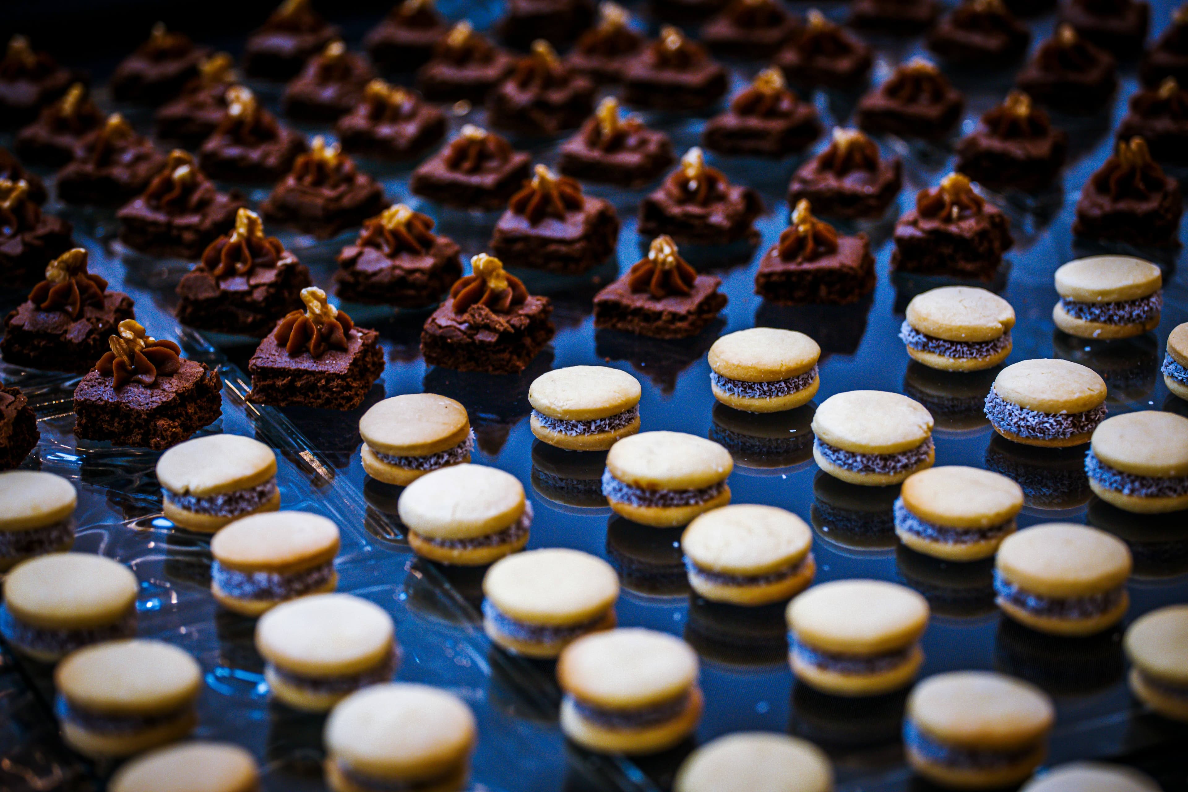 Rows of chocolate brownie bites and sandwich cookies on a dark reflective surface